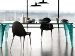 Mesa Atlas de vidrio con patas esculpidas, rodeada de sillas negras en un comedor moderno.