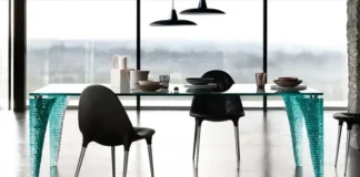 Mesa Atlas de vidrio con patas esculpidas, rodeada de sillas negras en un comedor moderno.